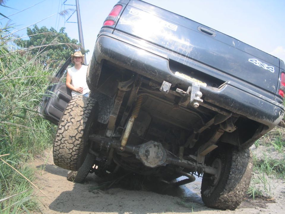 guy in hat next to black pickup truck stuck in mud, showing undercarriage and 4x4 decal