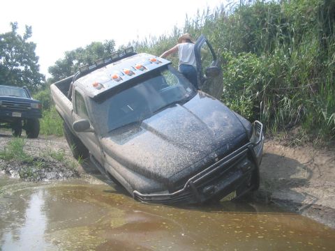 1990 Ford Bronco - A truck is stuck in the mud with another vehicle visible in the background.
