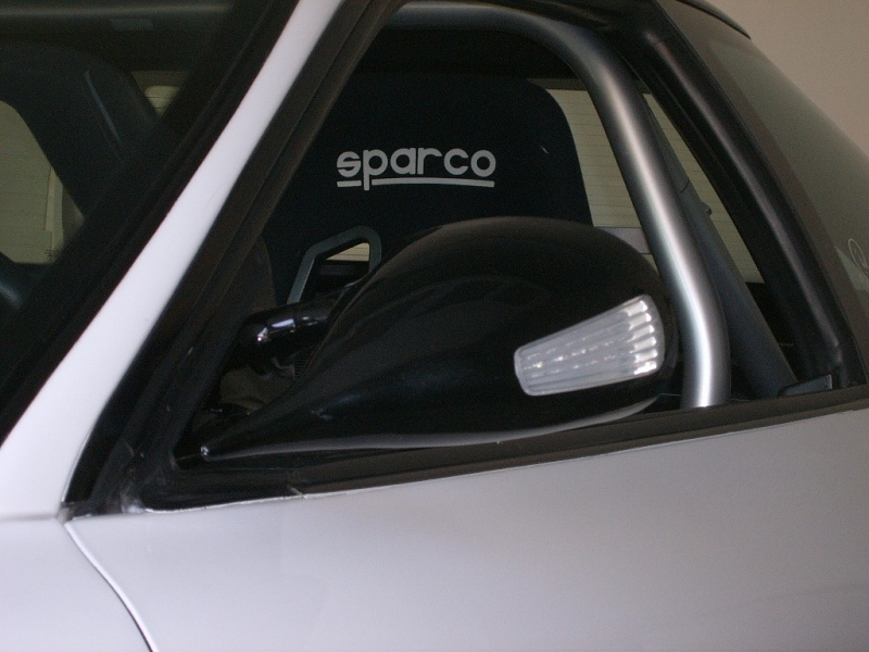 Car interior showing a Sparco racing seat and a black side mirror with integrated turn signal