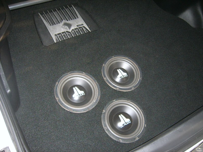 Car interior with three JL Audio subwoofers and an amplifier on black carpet