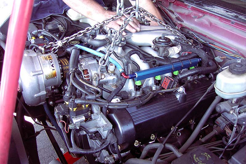 Supercharged V8 being lowered into a red car's engine bay on a hoist