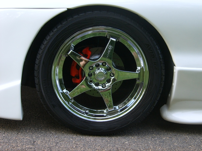 Chrome five-spoke wheels with orange brake calipers on a white car