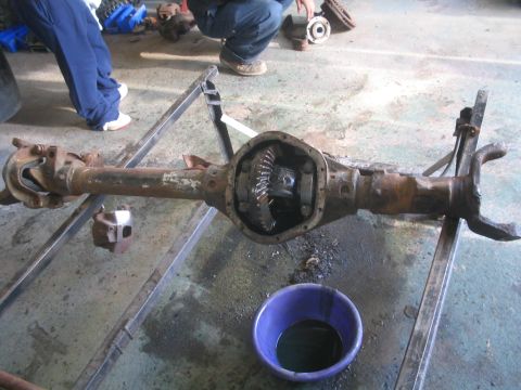 1990 Ford Bronco - Differential axle assembly on a stand, with a purple bowl of fluid nearby.