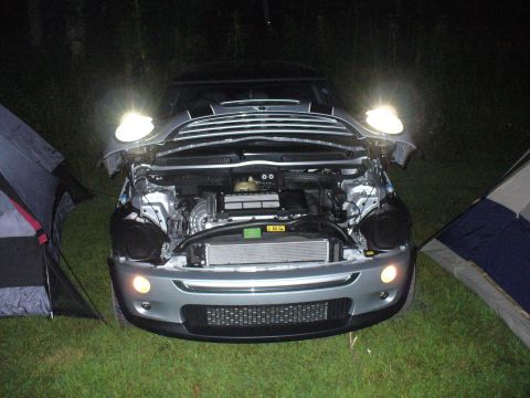 1991 Ford Probe - A silver Mini Cooper sits on grass at night with its hood open, revealing the engine, flanked by two tents.