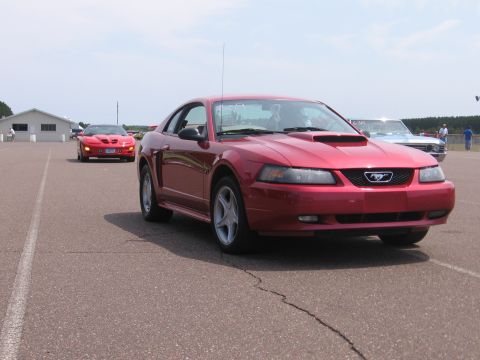 1989 Ford Mustang - Red Ford Mustang on asphalt with other cars in the background under a cloudy sky.