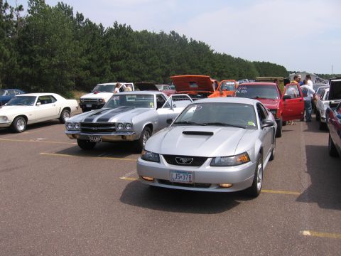 1989 Ford Mustang - A silver Ford Mustang is parked in a lot with other vehicles, including a classic muscle car.