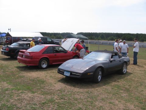 1989 Ford Mustang - A gray convertible sports car is parked on grass with other vehicles and people in the background.