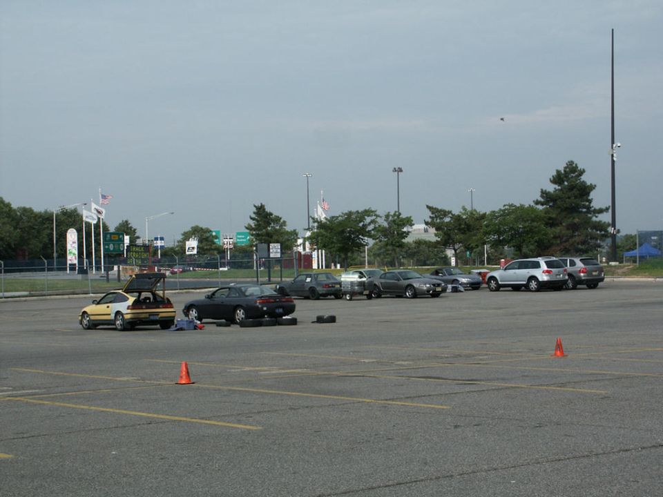 Parking lot with multiple cars, traffic cones, and a person lying on the ground near a yellow hatchback