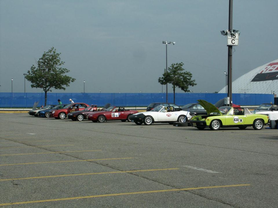 Several sports cars parked in a lot, including a red convertible with racing numbers and a lime green convertible with its hood open