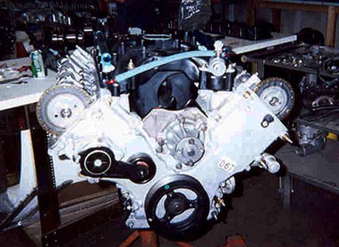 1992 Ford Crown Victoria - Front view of a freshly built Ford modular DOHC V8 engine on a stand in a workshop, with painted white cam covers, exposed cam sprockets an…
