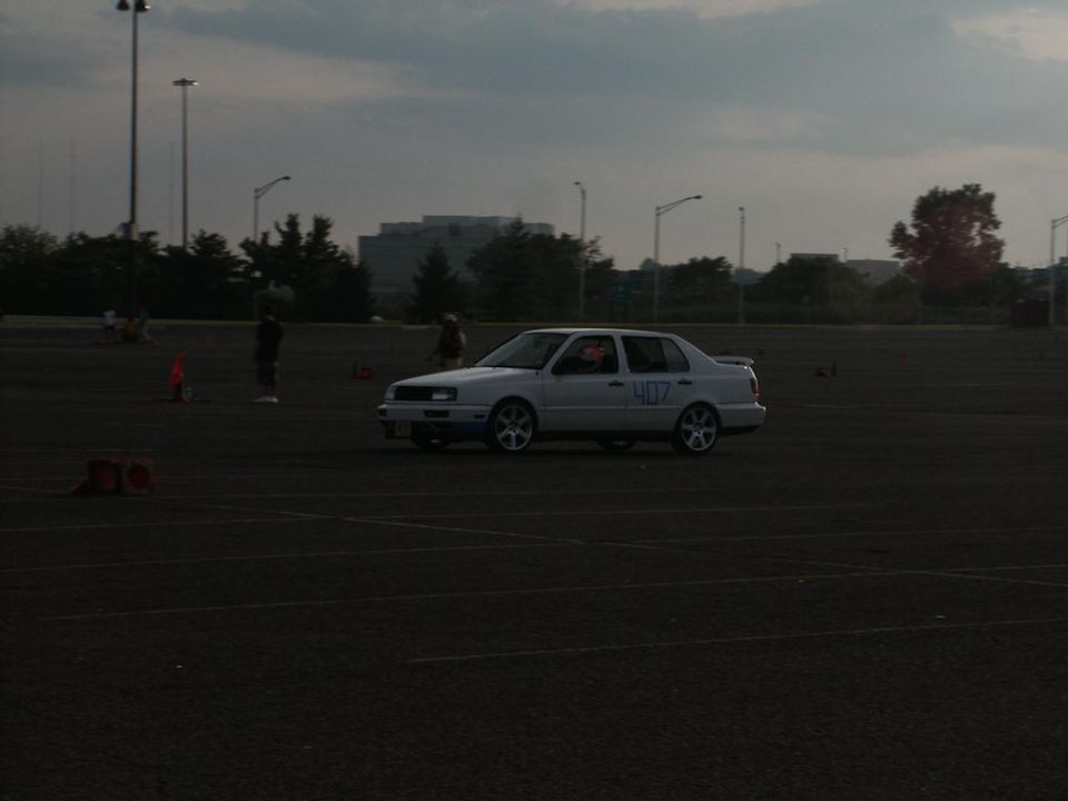 White sedan with racing number 407 on the door, seen from a 3/4 front angle on a dark asphalt lot