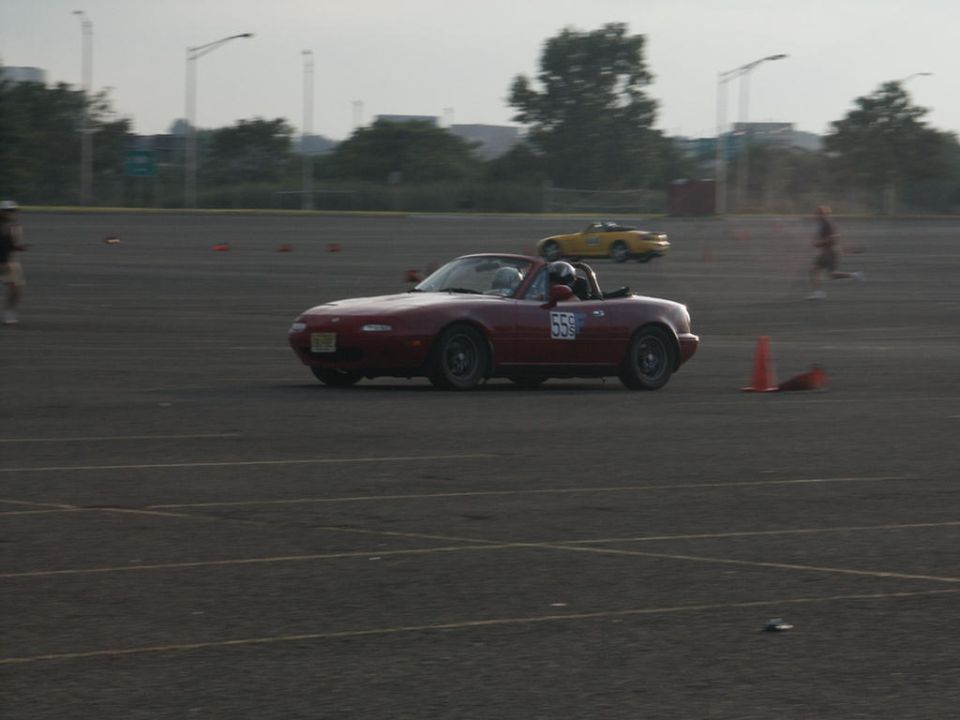 Red convertible sports car with number 559 on door, yellow convertible in background on a track