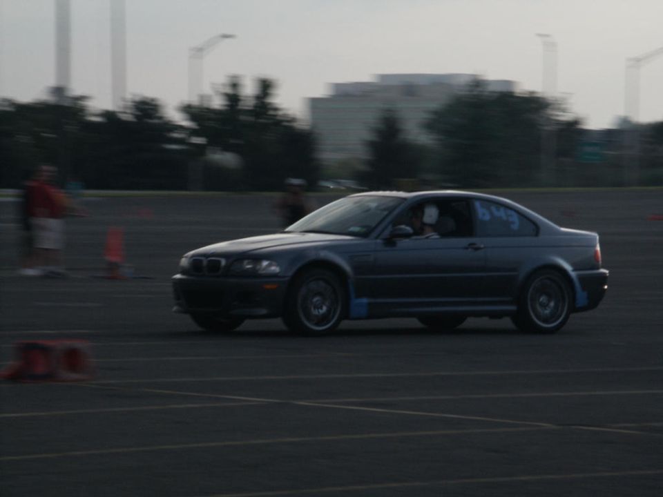 Dark coupe with racing numbers on door, driving on asphalt track