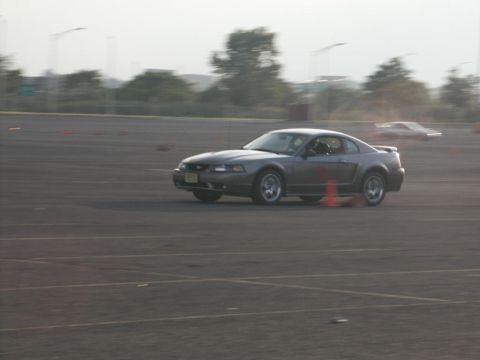 2001 Mercury Grand Marquis - A gray Ford Mustang navigates a track with orange cones, while another vehicle is visible in the distance.