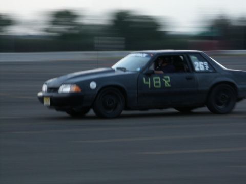 2001 Mercury Grand Marquis - A black 1987 Ford Mustang race car, identified by its body style, is seen in motion on a track with racing numbers displayed.
