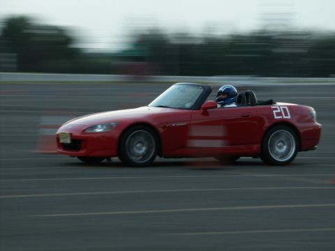 2001 Mercury Grand Marquis - A red convertible sports car with racing numbers speeds down a track, driver in a helmet visible.