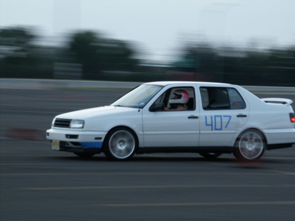White sedan with number 407 on the side, driver wearing a helmet, on a track