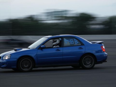 2001 Mercury Grand Marquis - Blue Subaru Impreza WRX sedan with racing numbers on the window, driving on a track.