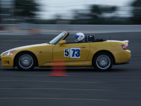 2001 Mercury Grand Marquis - A yellow convertible sports car with racing numbers is captured in motion on a paved track.