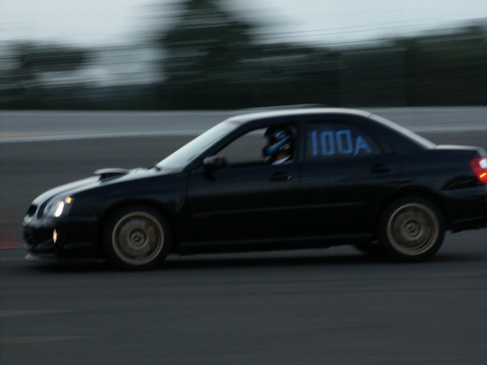 Black sedan with racing number 100A on the driver's side window, seen from the side at dusk