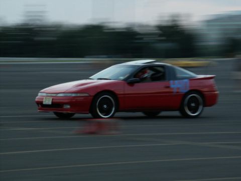 2001 Mercury Grand Marquis - A red coupe with blue markings on its side is captured in motion on a paved surface.