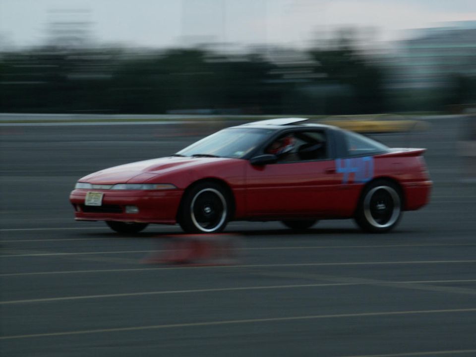 Red coupe with blue markings on the side, seen from the side at an angle, with motion blur