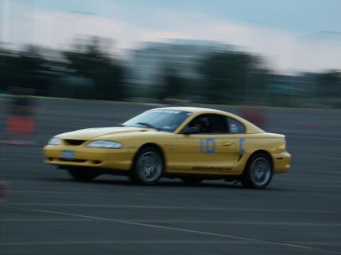 2001 Mercury Grand Marquis - Yellow Ford Mustang with racing numbers '10-C' on the door is seen on a track.