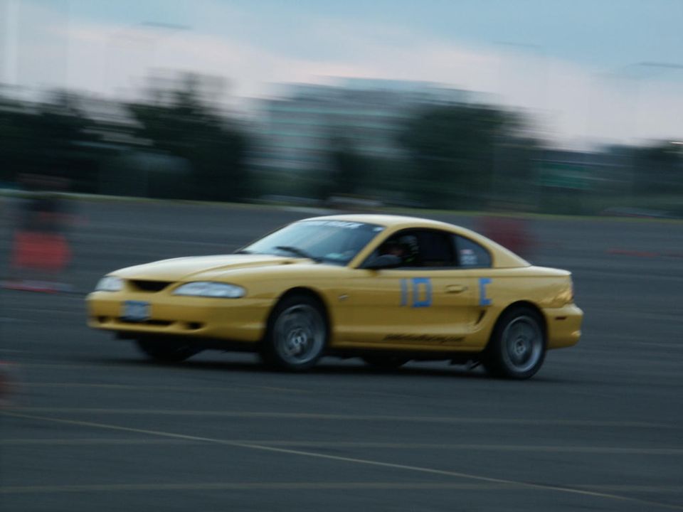Yellow Ford Mustang with racing numbers '10-C' on the door, seen from the side on a track