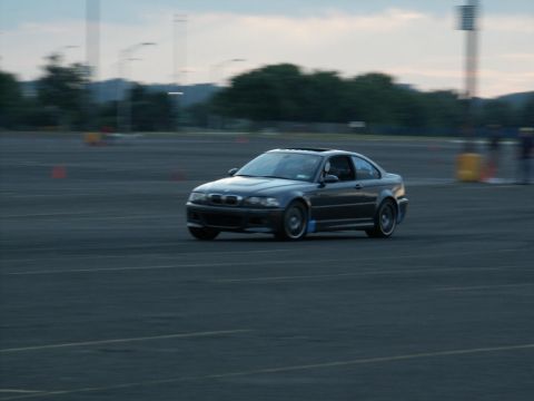 2001 Mercury Grand Marquis - A dark BMW M3 E46 coupe is captured in motion on an asphalt surface, with trees and poles visible in the background.