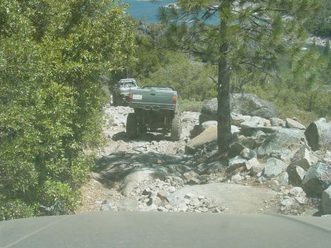 1986 Ford Bronco - Trail view over the photographer's own hood of a green lifted mini-truck ahead on a granite rock section, seen from behind with its bed emp…