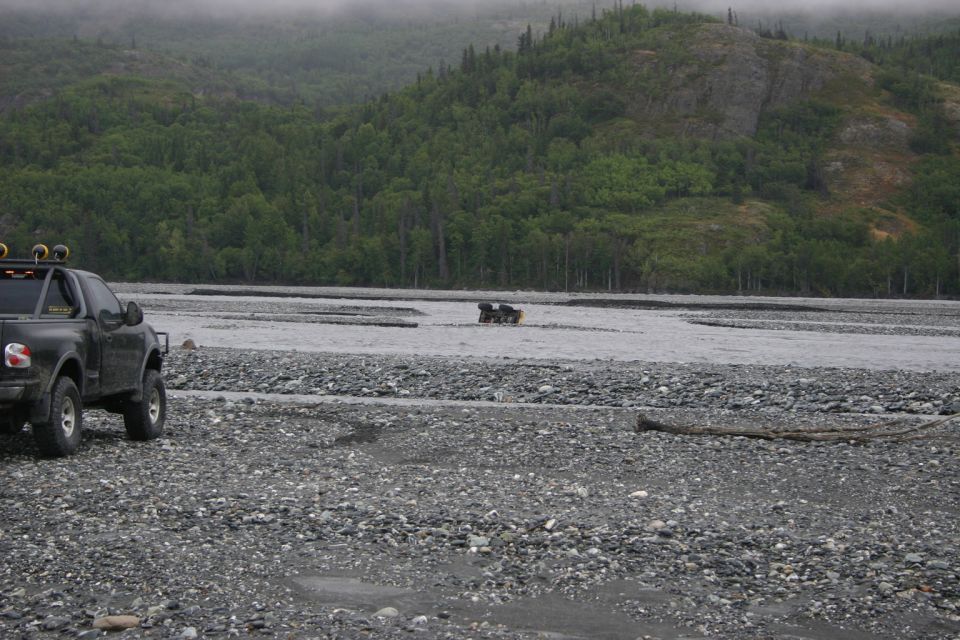 Black pickup truck on rocky riverbed with another vehicle in the water