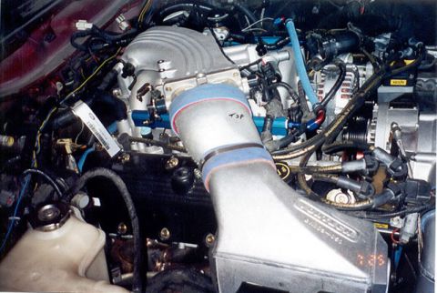 1992 Ford Crown Victoria - Close-up of a supercharged V8 engine bay showing a ribbed roots-style supercharger case and a large fabricated aluminum charge pipe joined…