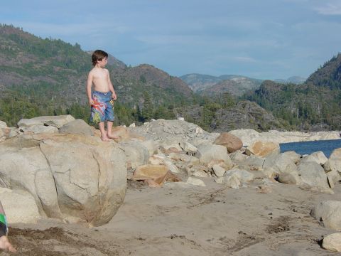 1986 Ford Bronco - A young boy surveys the rocky shoreline and distant mountains under a partly cloudy sky.