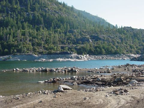 1986 Ford Bronco - A scenic view of a lake with a rocky shoreline and a dense forest covering the mountainside.