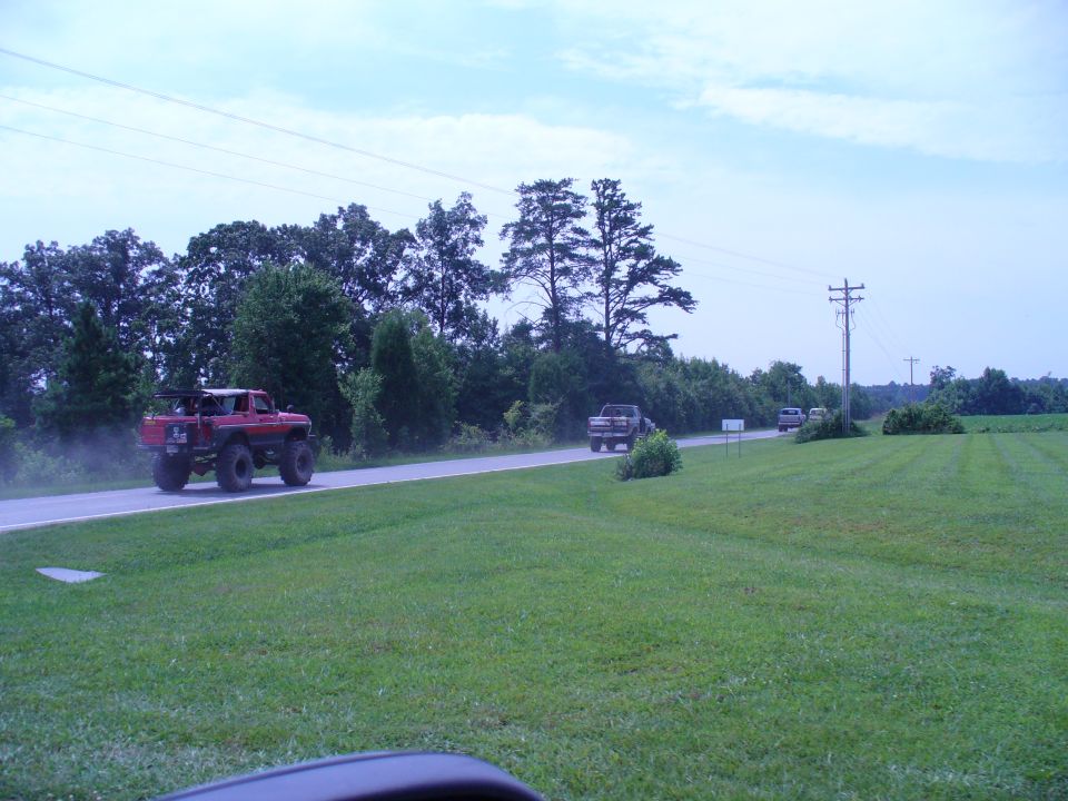 Red lifted truck with roll bar driving on a road, kicking up dust