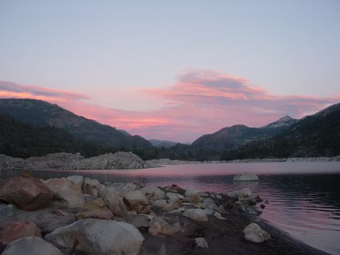 1986 Ford Bronco - Pink sunset over a granite-rimmed mountain lake, with boulders along the shoreline and forested ridges reflected in still water. No vehicle…