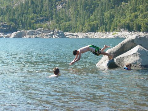 1986 Ford Bronco - A person dives into a lake while others swim, with a wooded hillside in the background.