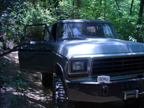 1996 Ford Bronco - A green Ford Bronco is parked on a dirt path in a wooded area, with the driver's door open.