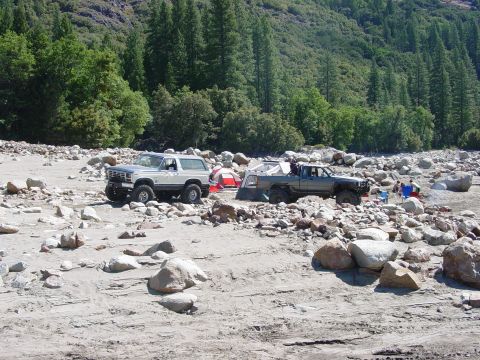 1986 Ford Bronco - A 1986 Ford Bronco and a pickup truck are parked in a dry riverbed, set up for camping with tents and chairs.