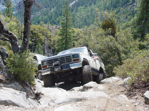 1986 Ford Bronco - This 1980s Ford Bronco is tackling a challenging rocky trail in a mountainous, wooded area.