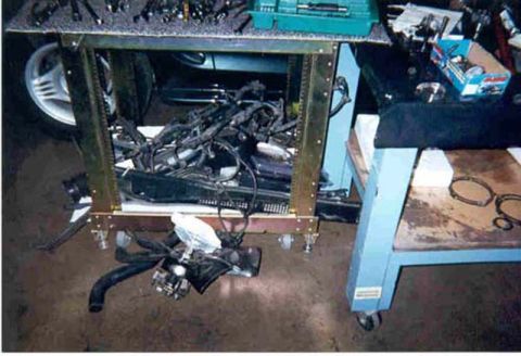 1992 Ford Crown Victoria - A garage floor scene during a teardown, with a removed engine wiring harness and loom coiled under a metal shop table and a throttle body w…