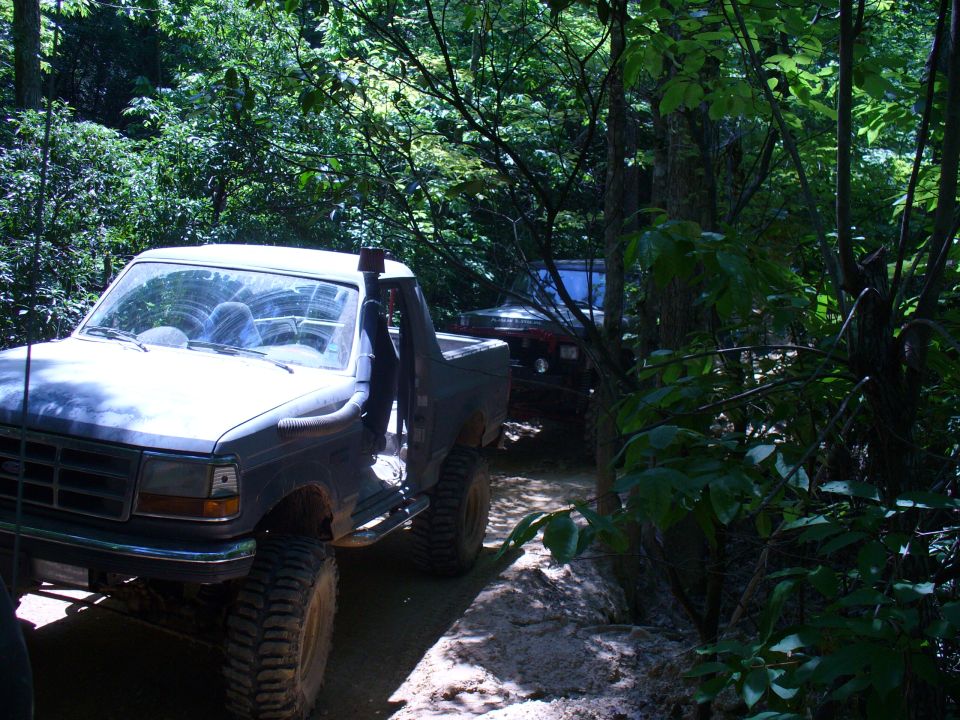 Dark blue Ford Bronco with snorkel, off-road tires, and lifted suspension on a dirt trail