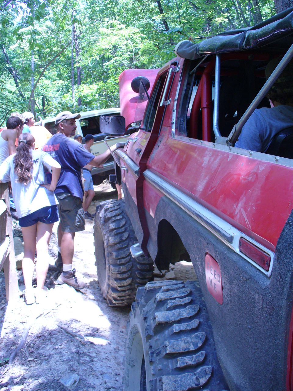 Red off-road vehicle's side view with large tires and roll cage. "FEED ME" sticker visible