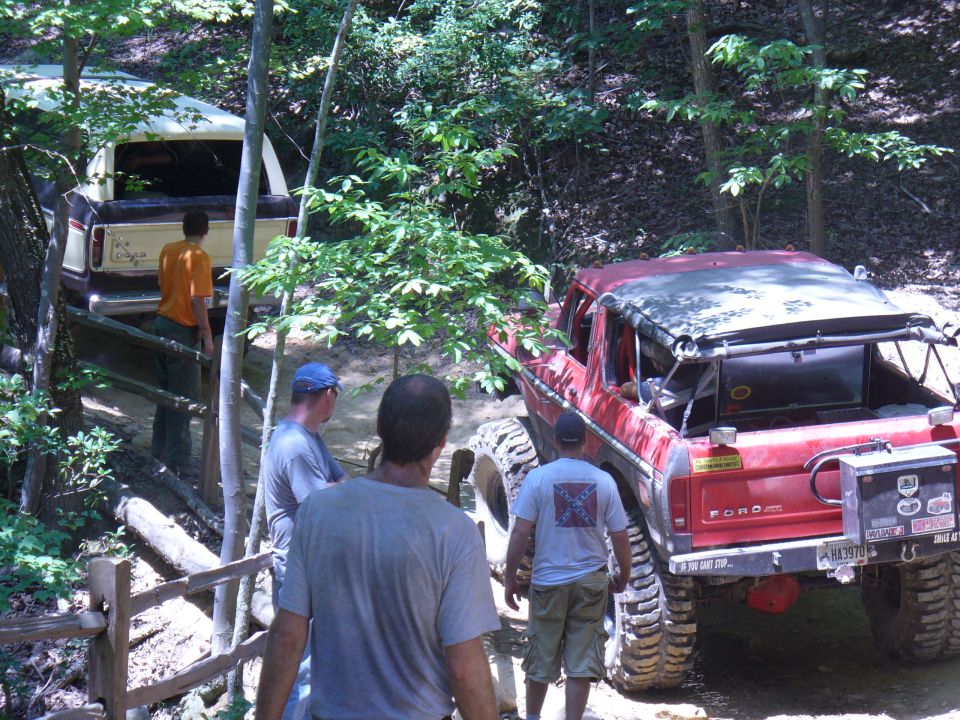 Red Ford Bronco and a tan Ford Bronco on a wooded trail with people around