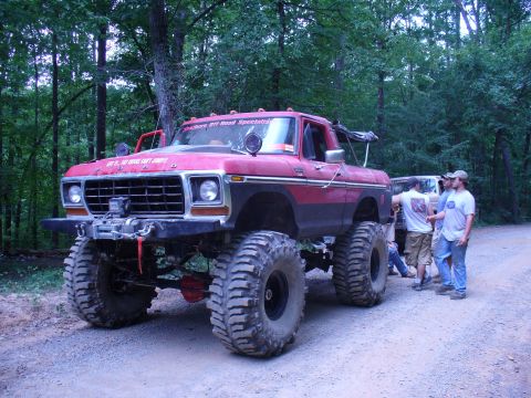 1996 Ford Bronco - A heavily modified red pickup truck sits on a dirt road surrounded by trees, with several people standing nearby.