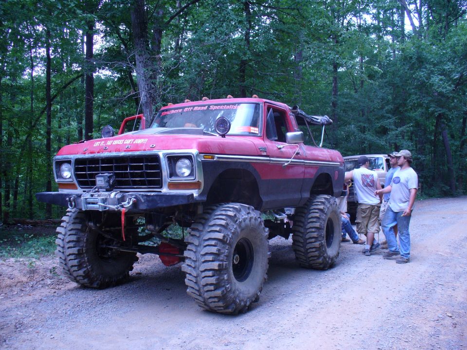 Red lifted pickup truck with large tires and winch, parked on a dirt road