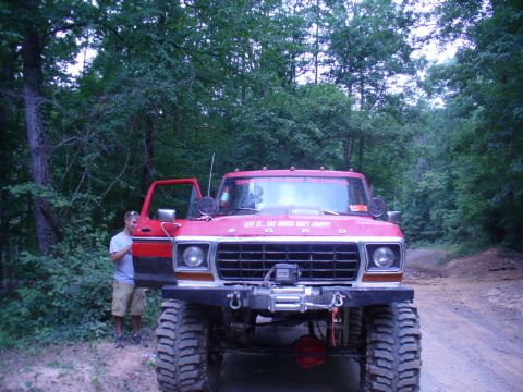 1996 Ford Bronco - Modified red Ford pickup truck with off-road tires and winch is parked on a dirt road.
