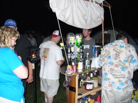1991 Ford Probe - An outdoor bar is set up with various bottles and a blender, serving drinks to people at night.