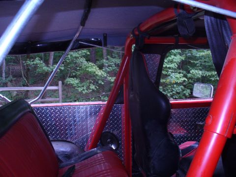 1996 Ford Bronco - The interior of a modified off-road vehicle shows red seats and a prominent red roll cage against a backdrop of trees.