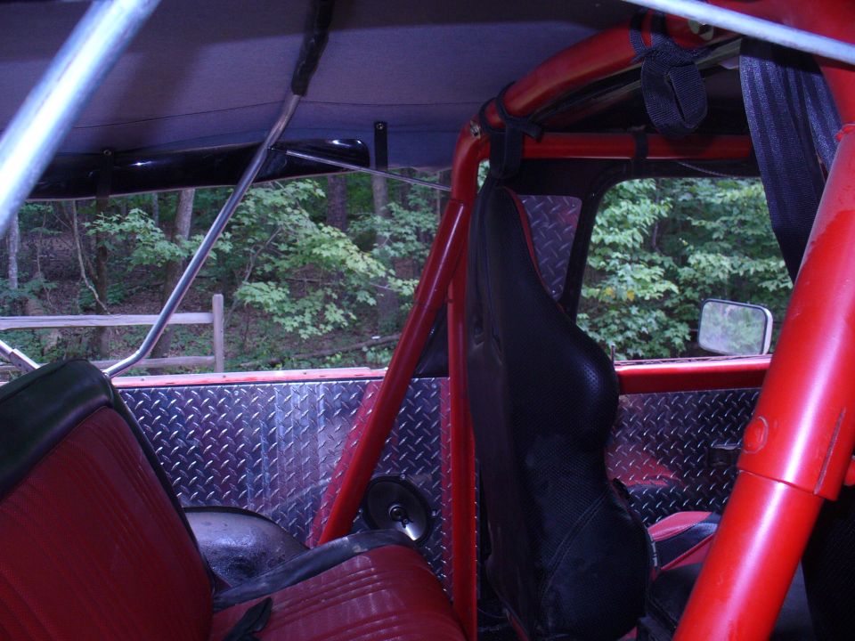 Inside of a red off-road vehicle with roll cage, diamond plate panels, and red seats. Trees and a wooden fence visible through the window